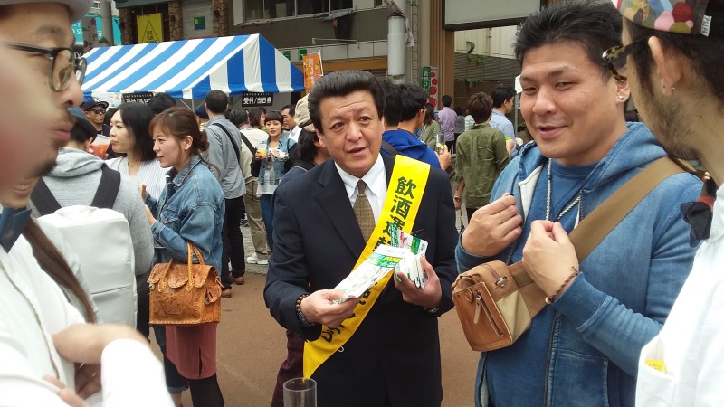 会場内の来場者に代行利用方法を説明する会員 